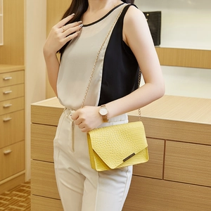 Detail of yellow crocodile pattern bag with metal buckle and gold chain strap on model