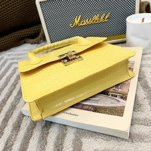 Detail of yellow crocodile pattern handbag with golden square lock and accordion sides