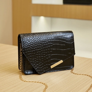 Detail of black crocodile embossed leather crossbody bag with elegant gold chain strap