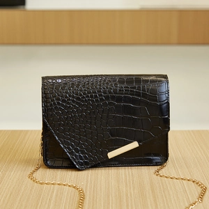 Detail of black crocodile texture bag with gold metal trim and chain strap