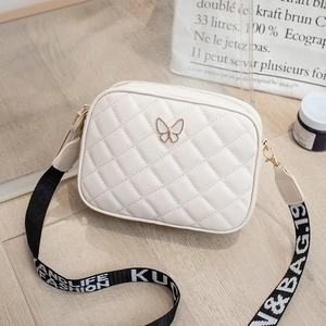 Detail of white quilted camera bag with butterfly clasp and fashion printed strap