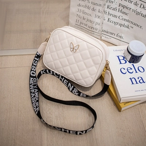 Detail of white quilted crossbody bag with golden butterfly clasp and printed wide strap