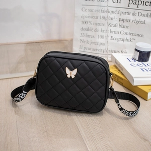 Detail of black quilted camera bag featuring a white butterfly buckle and wide strap