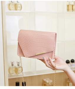 Close-up of pink croc-embossed leather texture with gold metal chain and trim details
