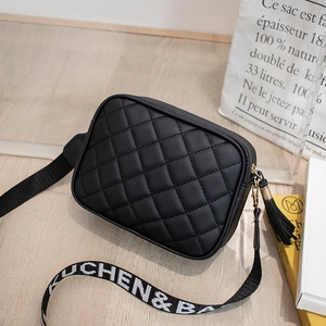 Detail of black quilted camera bag with woven logo strap and decorative leather tassel
