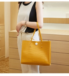 Detail of yellow crocodile pattern tote bag with white round button on a female model