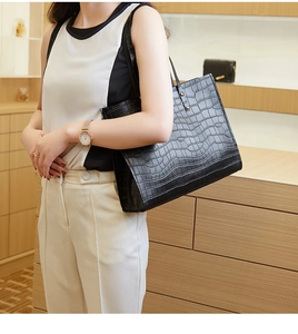 Detail of black crocodile-embossed tote bag featuring textured pattern and slim handles