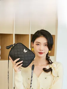 Close-up of black quilted crossbody bag with gold butterfly charm and tassel detail