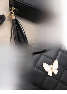 Detail of black quilted camera bag featuring a metal butterfly charm and long tassel