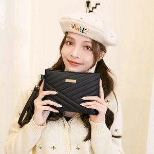 Detail of black quilted leather envelope clutch bag with gold hardware and wrist strap