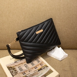 Detail of black quilted leather clutch featuring golden logo plate and wristlet strap