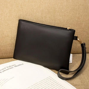 Close-up of black leather clutch bag with gold zipper on a vintage book