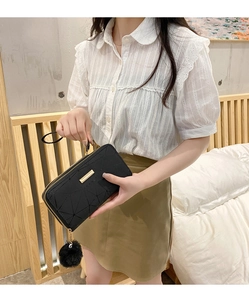 Detail der schwarzen gesteppten Clutch mit Goldbeschlägen und flauschigem Bommel-Anhänger