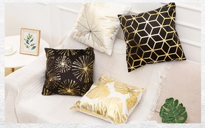 Detail of four black and gold plush pillows with geometric and tropical leaf patterns