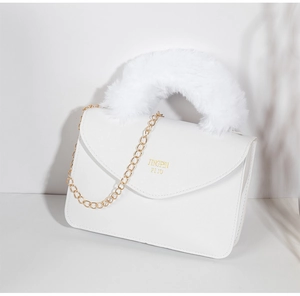Close-up of white faux fur handle and gold chain on textured leather handbag