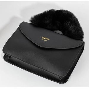 Detail view of the black crossbody bag featuring faux fur handle and gold logo print