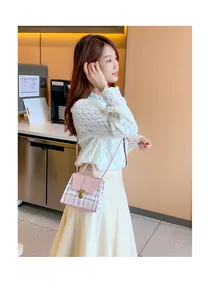 Close-up of pink plaid crossbody bag with gold metal lock worn by a woman in a cafe