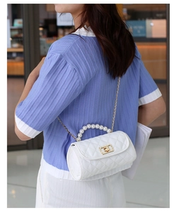 Detailed shot of a white quilted cylinder bag featuring pearl handle and gold chain strap