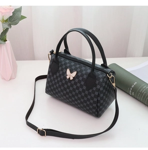 Detail view of a black Boston bag with geometric texture and white butterfly metal accent