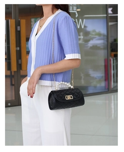 Close-up of black quilted bag with pearl handle and gold chain worn by a model