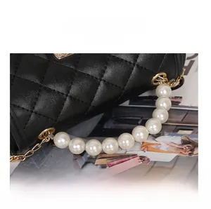 Detail of black quilted handbag with elegant pearl handle and gold chain accents