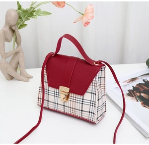 Detail of red leather and plaid patchwork crossbody bag with gold buckle on white table