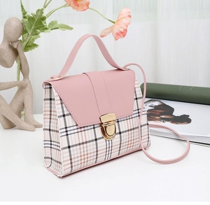 Detail of pink plaid mini crossbody bag with metal lock and handle on minimalist desk