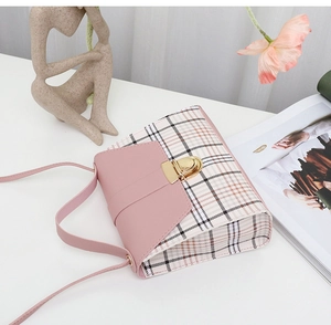 Pink checkered mini crossbody bag with gold buckle on white surface near flowers
