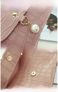 Détails de la texture crocodile, du charme perle et du fermoir magnétique du sac rose