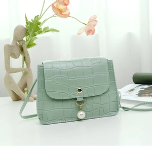 Détail du sac vert clair à texture crocodile avec boucle dorée et perle pendante