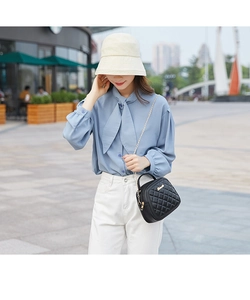 Outdoor street shot of a black quilted crossbody bag with gold chain and logo plaque