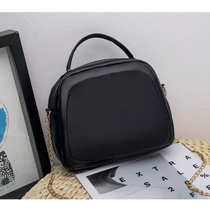 Detail of black crossbody bag with litchi texture and golden chain strap on stylish background