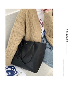 Close-up of black lychee grain leather tote bag with tassel charm and gold magnetic closure