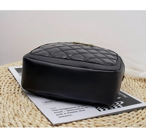 Detailed side view of black quilted crossbody bag with gold metal plate on top
