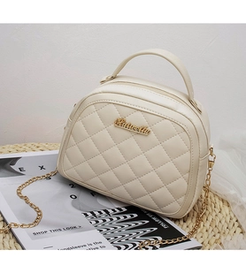 Detail of beige quilted crossbody bag with gold logo plate and chain strap on stylish decor