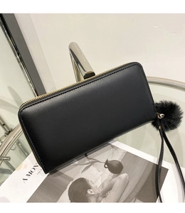 Detail of black pebbled leather long wallet with golden zipper and fluffy fur pompom charm