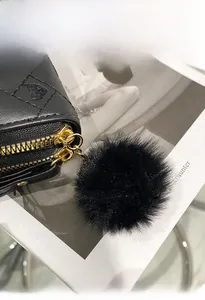 Close-up of black quilted wallet featuring double gold zippers and a soft fur ball pendant