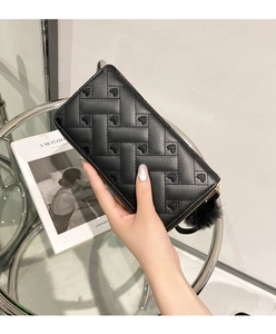 Close-up of black long wallet with heart embossed pattern and fluffy pompom keychain