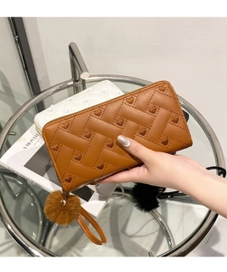 Close-up of woven long wallet with heart embroidery and plush pom-pom keychain detail