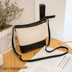 Sac seau bicolore matelassé en crème et noir posé sur une table en bois