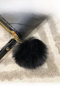 Detail of black quilted leather purse featuring a fluffy wool ball pendant and gold zipper