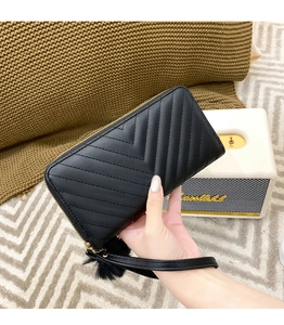 Detail of black V-quilted long clutch bag with wrist strap and soft faux fur pompom