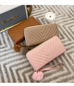 Macro detail of V-quilted women's long wallets with hand straps and plush pompom charms
