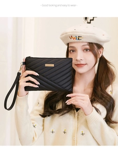 Detail of black quilted PU leather clutch bag with golden metal trim and wristlet strap