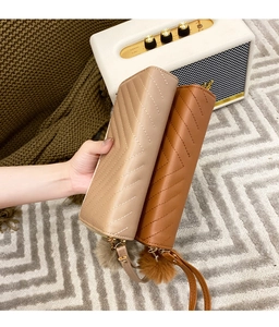 Detail of V-quilted long wallets in beige and orange with wristlets and pom-pom charms