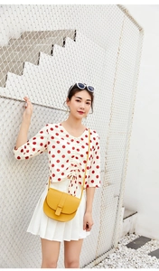 Crossbody yellow saddle bag styled with white polka dot top and pleated skirt