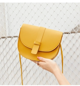 Detail view of ginger yellow leather saddle bag with strap and ring buckle closure