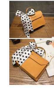 Detail of yellow crossbody bag with gold chain and black polka dot silk scarf handle