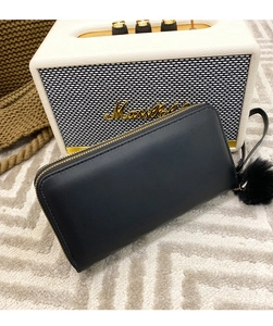 Close-up of black long leather wallet with gold zipper and a soft faux fur pompom charm