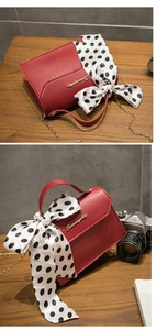 Detail of red leather crossbody bag featuring a golden chain and polka dot scarf handle